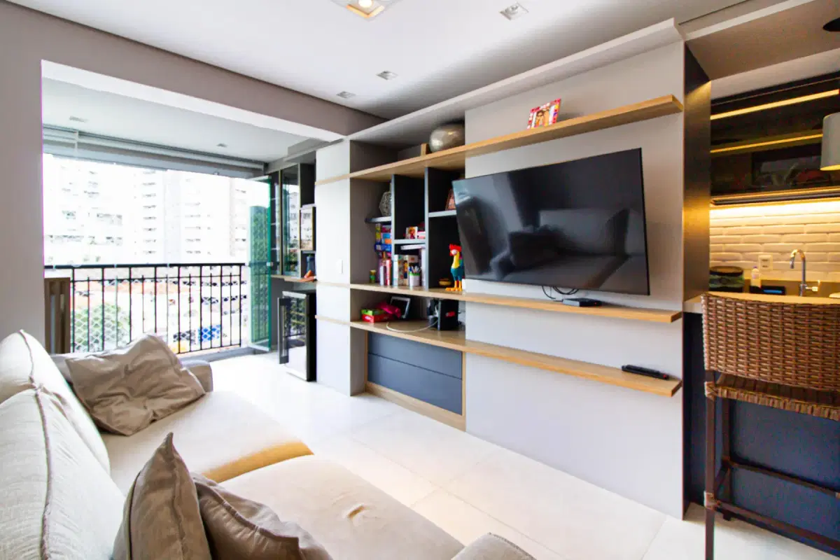 sala com estante de madeira, TV e varanda com vista de prédios
