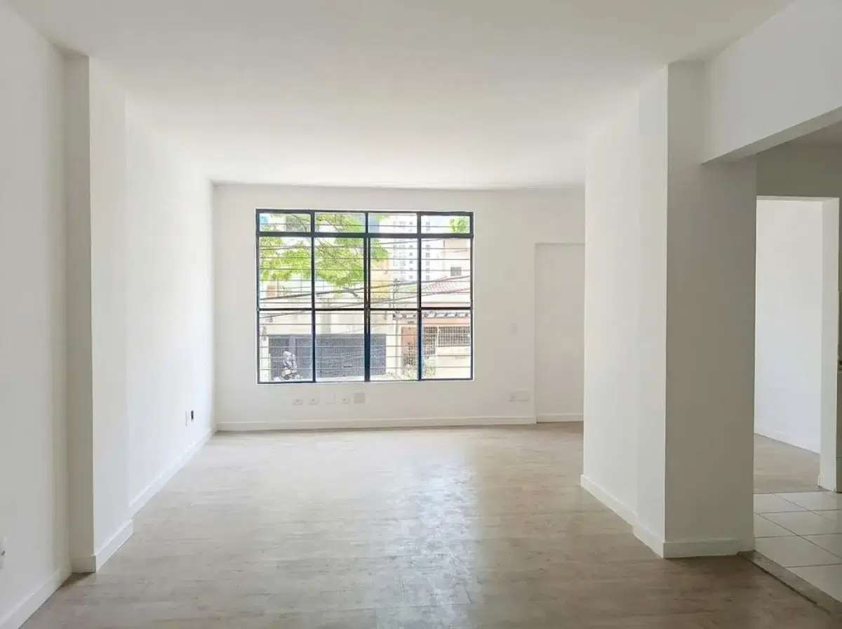 Sala ampla com parede branca, piso de madeira clara, janelas grandes