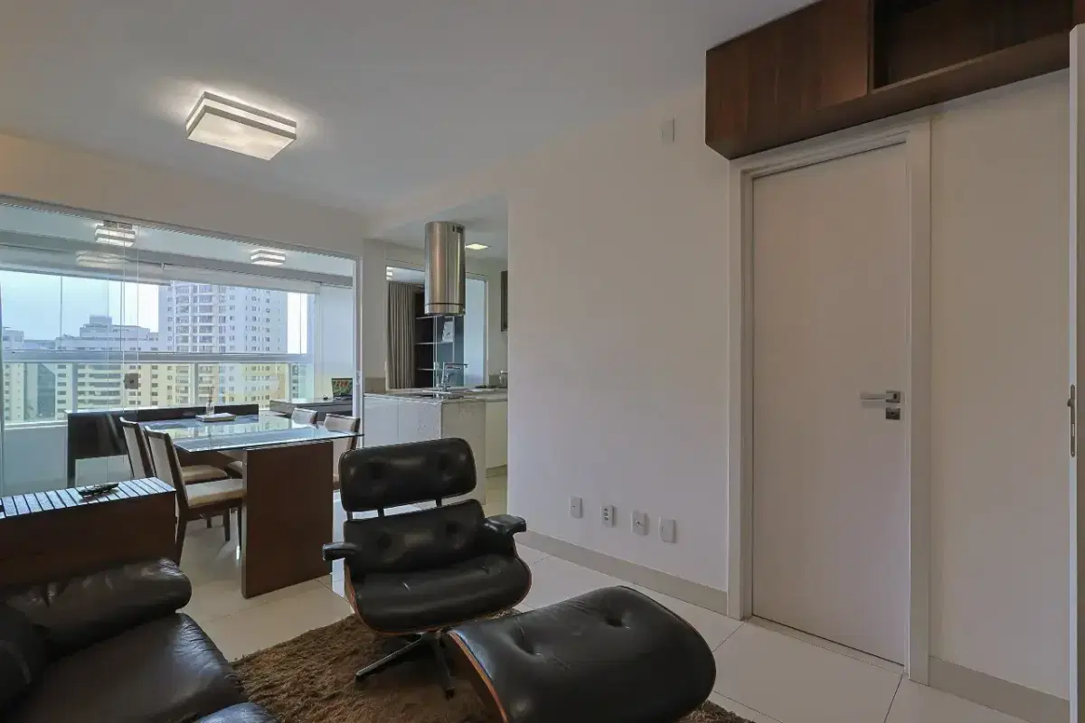 Sala com paredes brancas, móveis em couro preto, cozinha ao fundo