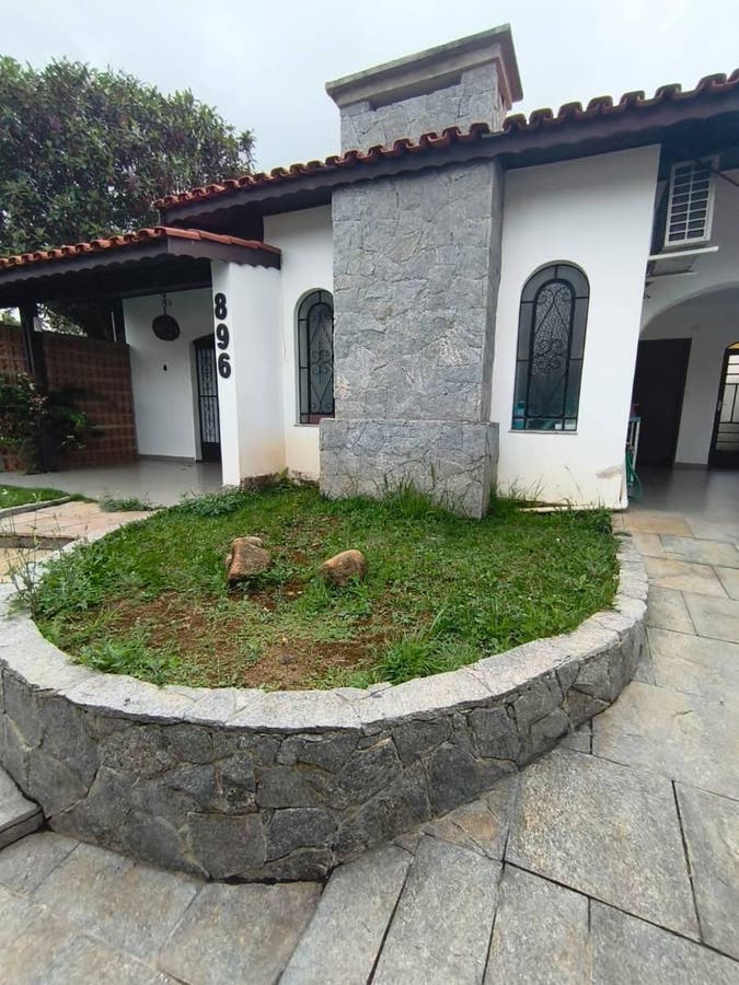 Fachada de casa com paredes brancas, janelas de vidro e cobertura de telhas vermelhas.