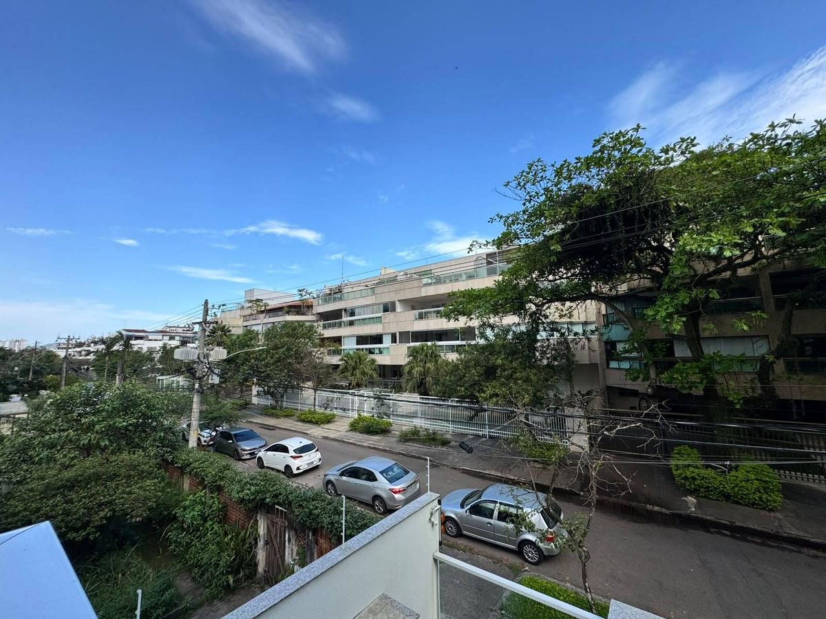 Rua residencial com prédio moderno, árvores e carros estacionados.