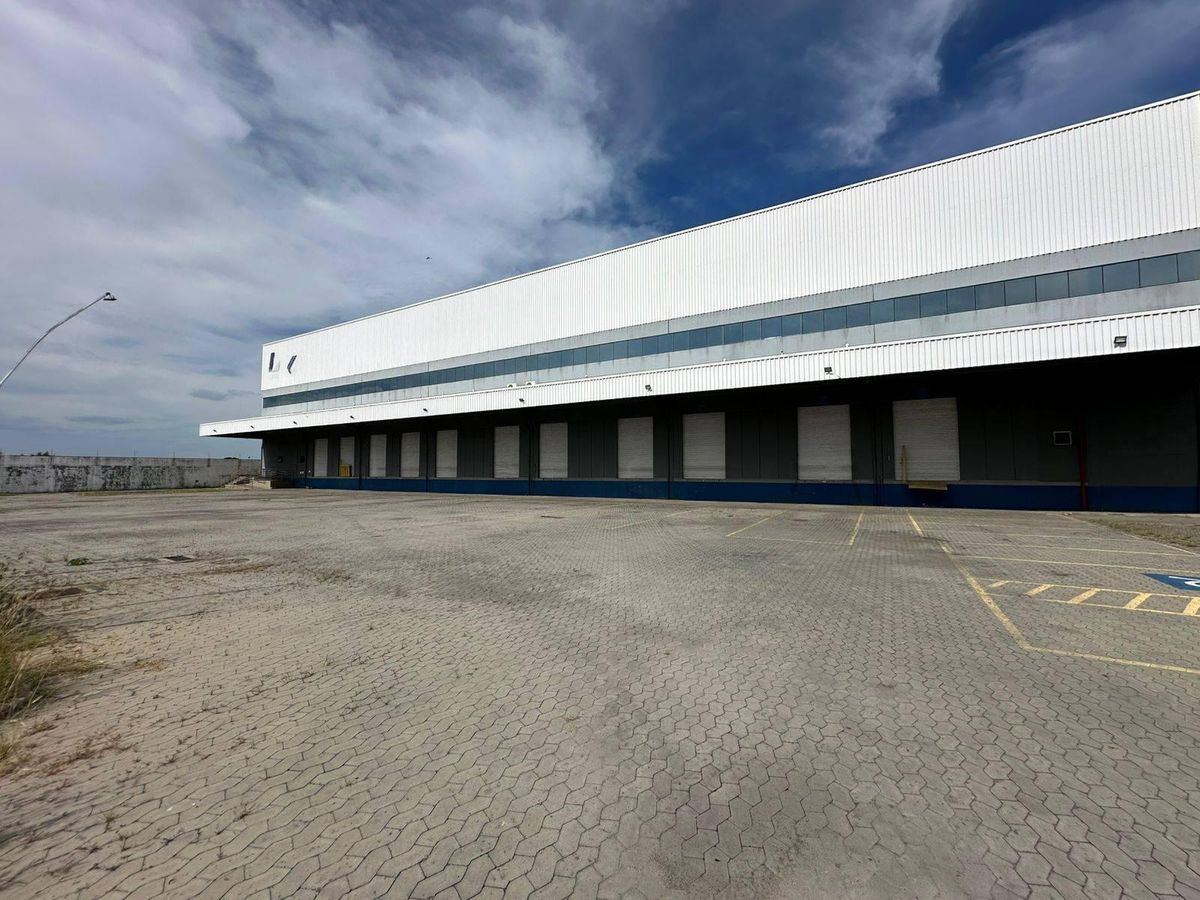 Edifício industrial com fachada de metal e janelas amplas, céu parcialmente nublado