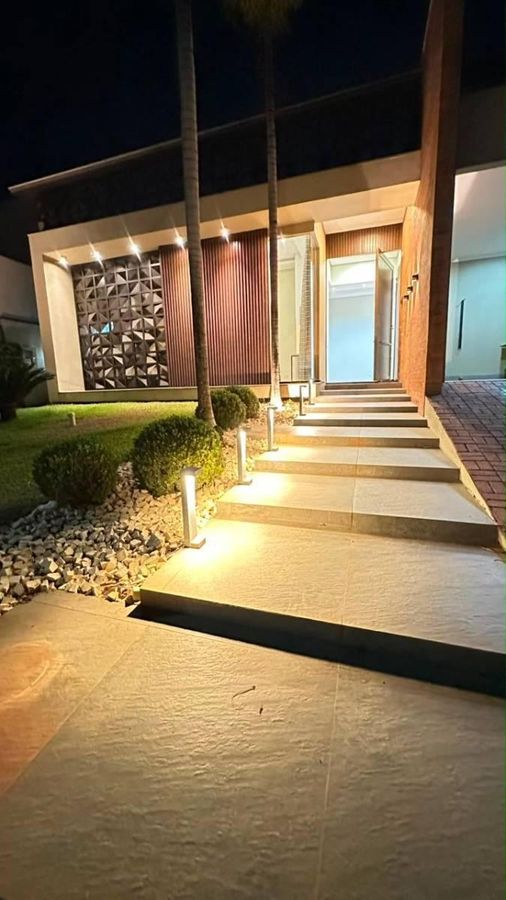 Entrada de residência moderna com iluminação externa, jardim bem cuidado.