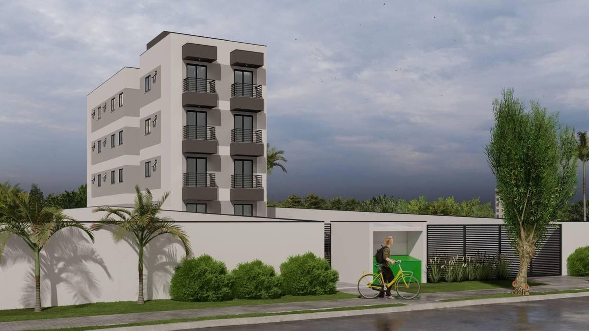 Prédio de apartamento de cinco andares com varandas e muro branco.