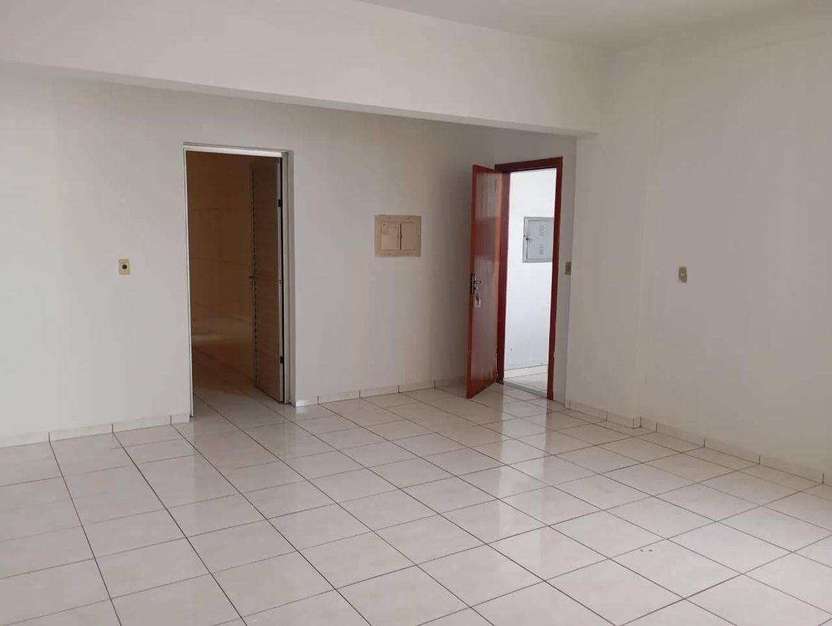 Sala vazia com paredes brancas, piso de cerâmica, porta de entrada e varanda.