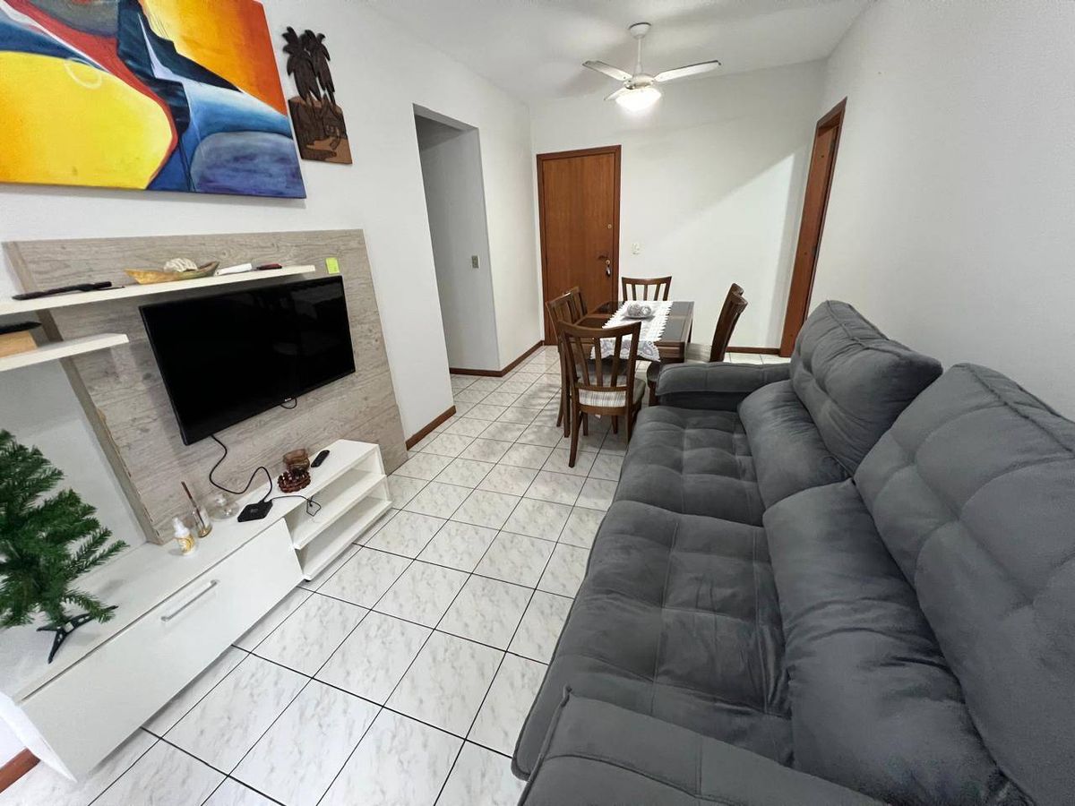 Sala com piso de cerâmica, paredes brancas, sofá cinza e televisão