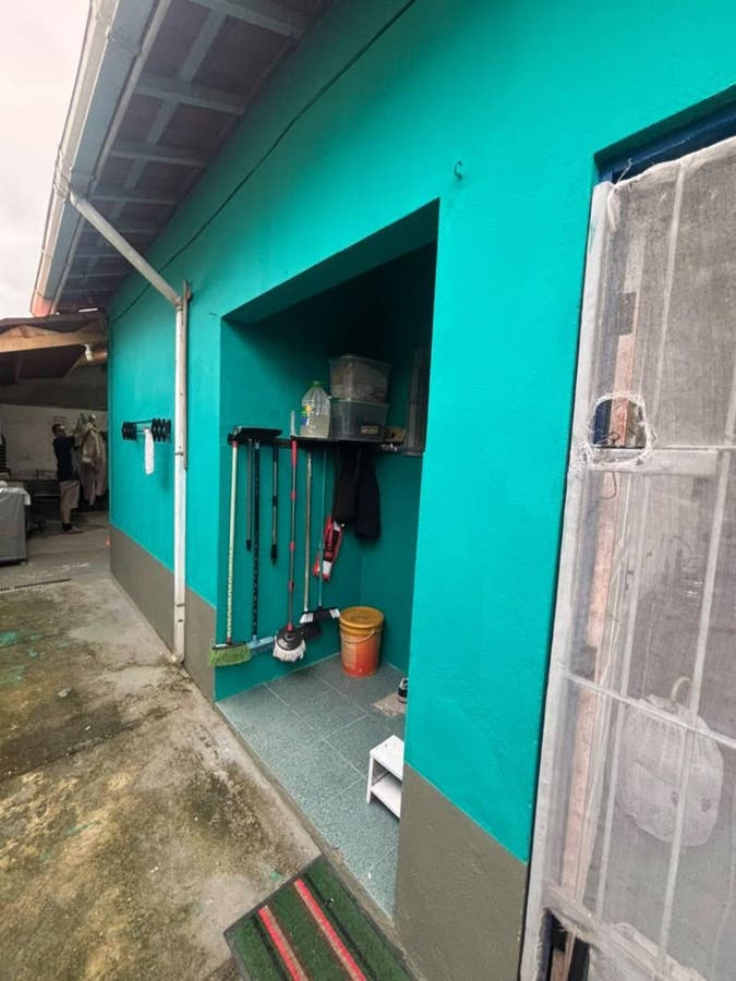 Área externa de casa com parede azul e objetos de limpeza pendurados