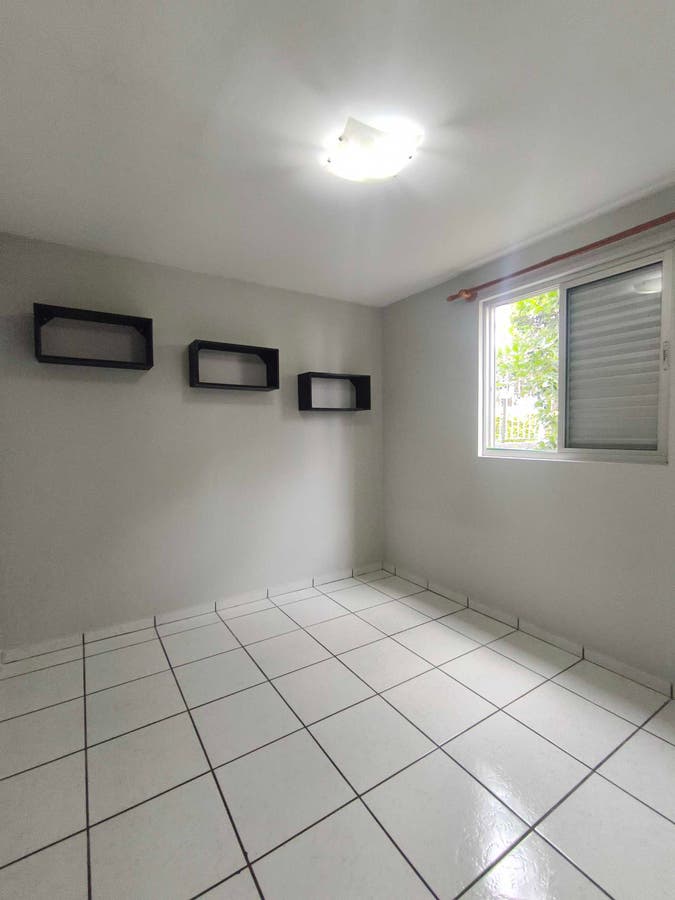 quarto com paredes brancas, piso de cerâmica e janela com cortina
