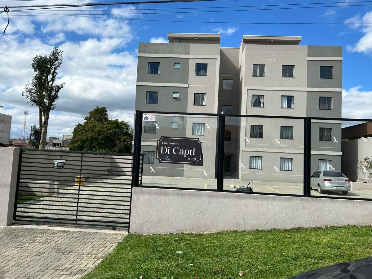 Prédio residencial cinza com janelas médias em rua com céu azul