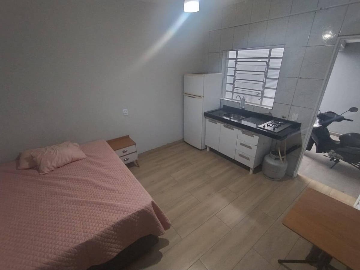 Quarto com cama, cômodo de parede lisa, cozinha integrada, janela de grades.
