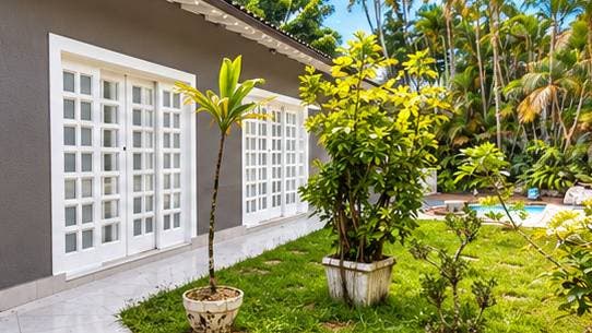 Jardim lateral com plantas em vasos e parede cinza com janelas