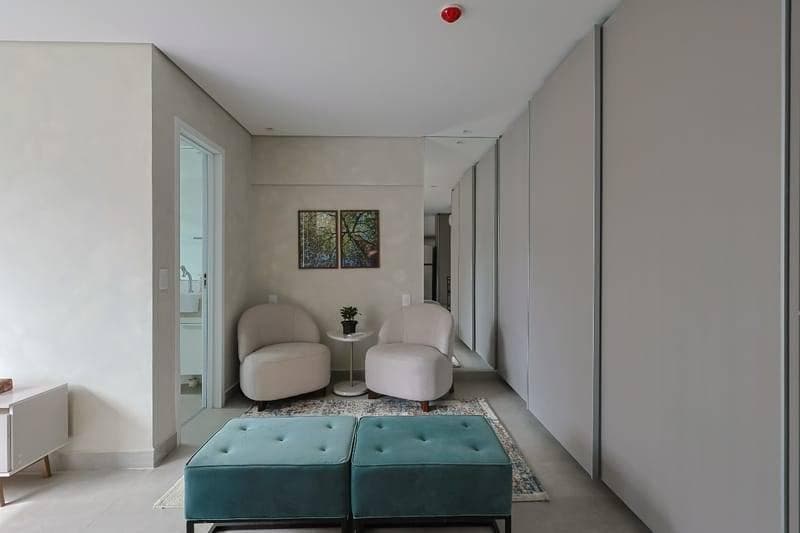 Sala com paredes claras, dois sofás curvos, armários brancos e quadro