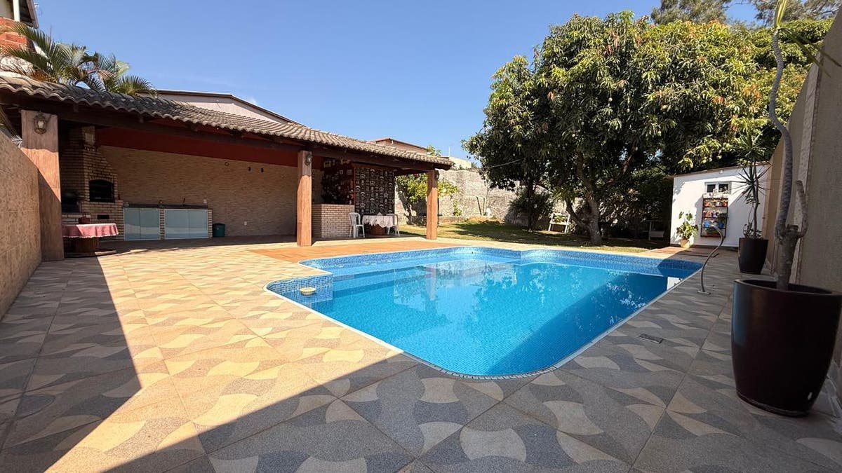 Piscina em área externa com piso decorativo, árvores e estrutura coberta