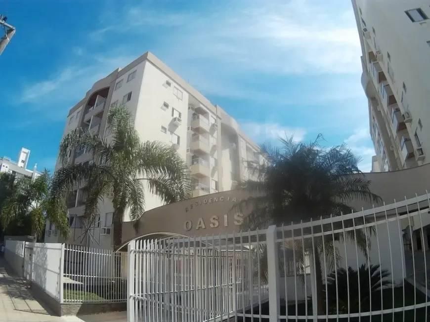 Prédio residencial alto com fachada branca, cercado por árvores e alambrado.
