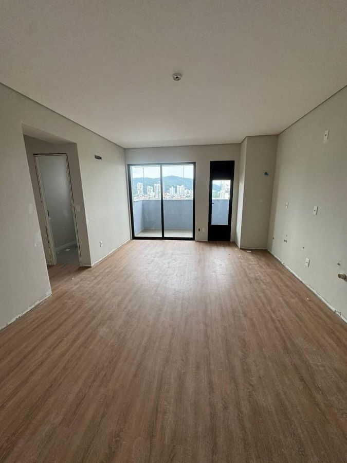 Sala vazia com piso de madeira, janelas de vidro e varanda.