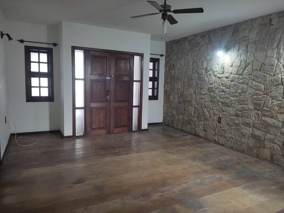 Sala com fachada de pedra, piso de madeira, janelas com persianas pretas