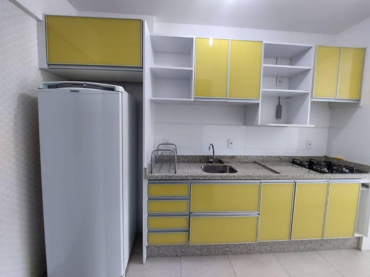 Cozinha com armários amarelos, pia e fogão embutido, parede branca.