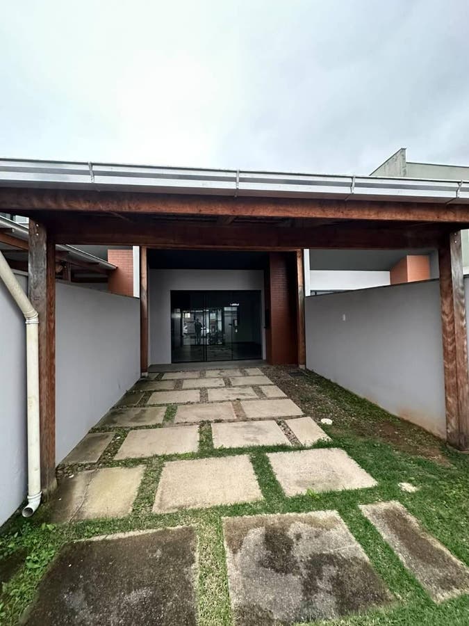 Entrada de residência com caminho de concreto, estrutura de madeira e muro.