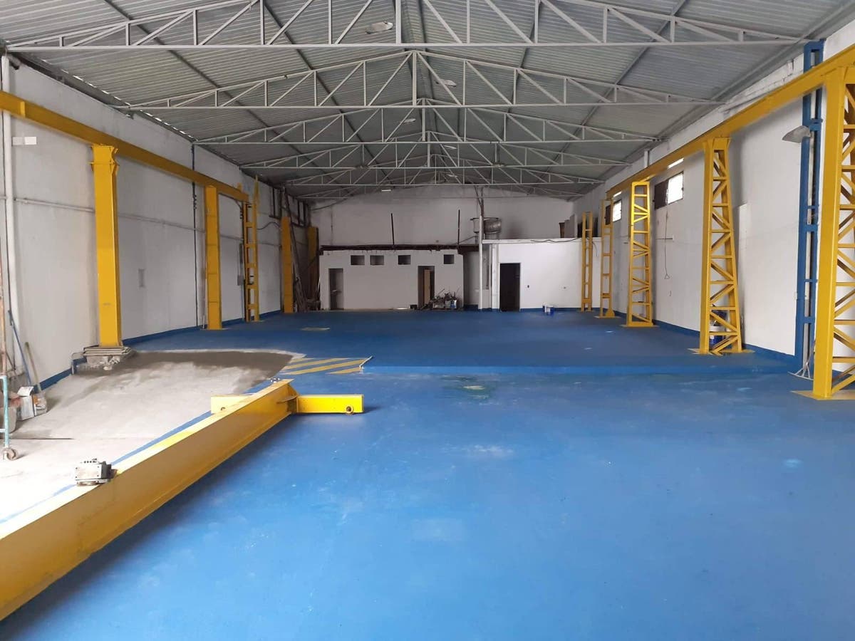 Espaço industrial com estrutura metálica, chão azul e paredes brancas.