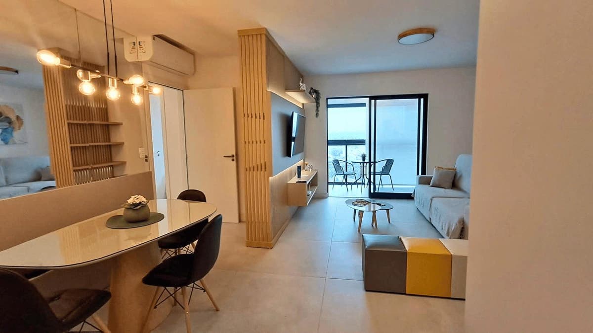 Interior de apartamento com sala, cozinha e varanda com vista urbana.
