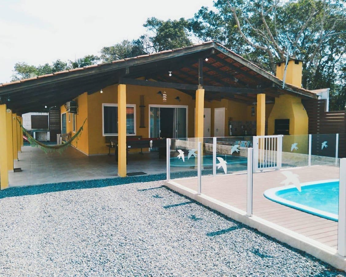 Casa amarela com varanda coberta, área de piscina e jardim externo
