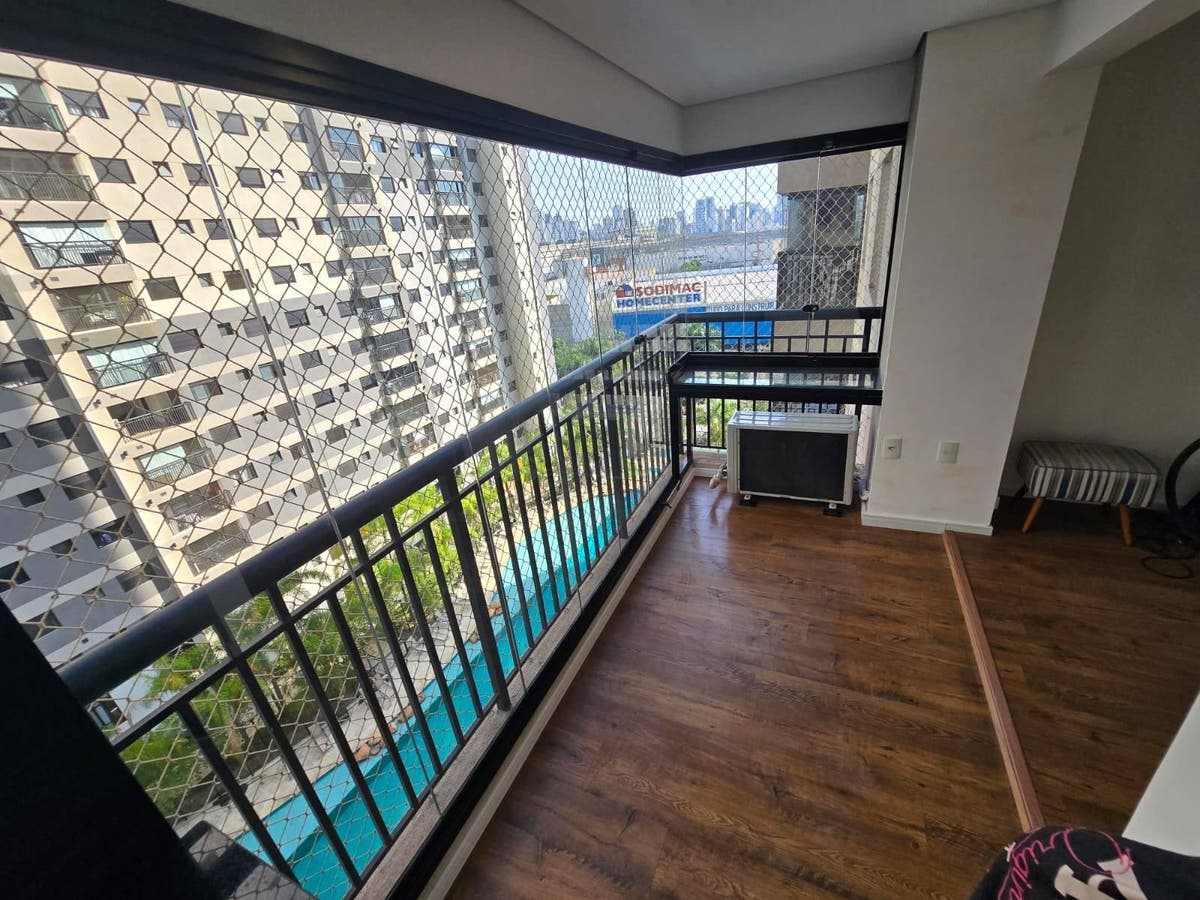 Varanda com piso de madeira, guarda-corpo de metal, vista para prédios e piscina