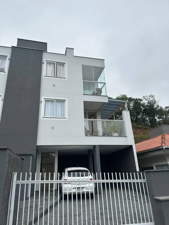 Prédio residencial de três andares com fachada branca e cinza, garagem coberta.