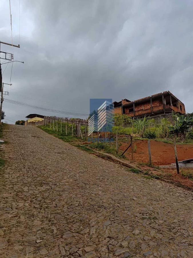 Estrada de pedra com casa em construção e vegetação ao redor.