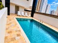 Piscina em área de lazer com cadeiras ao redor e prédio ao fundo