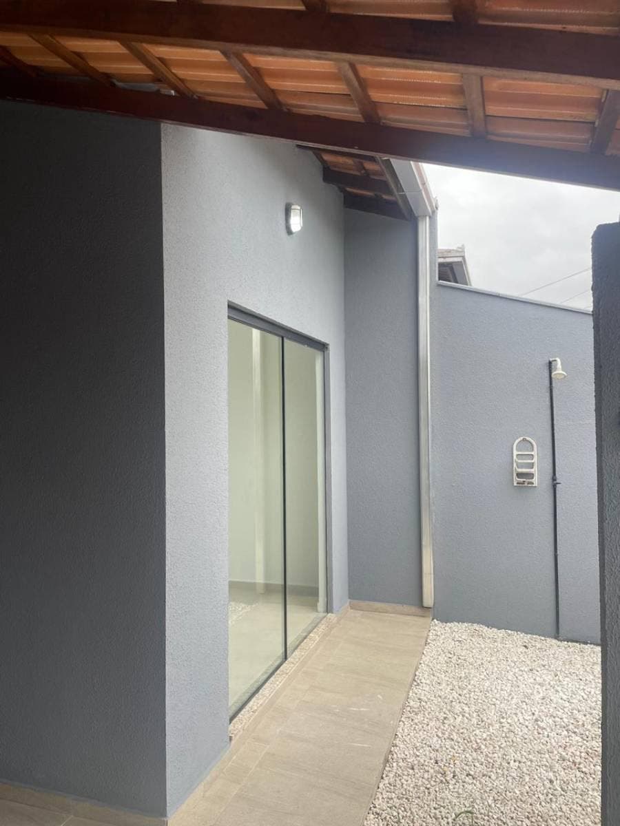 Fachada de casa com paredes cinzas, porta de vidro e teto de madeira.