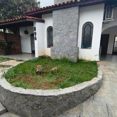 Fachada de casa com paredes brancas, janelas de vidro e cobertura de telhas vermelhas.