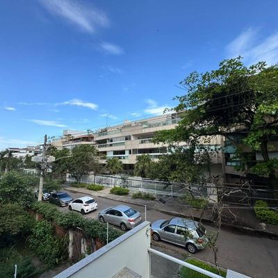 Rua residencial com prédio moderno, árvores e carros estacionados.