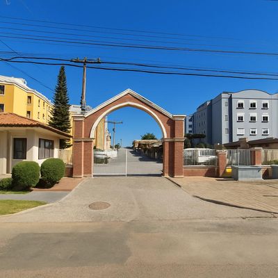 Entrada de condomínio com portal de tijolos, pavimentação e prédios ao fundo