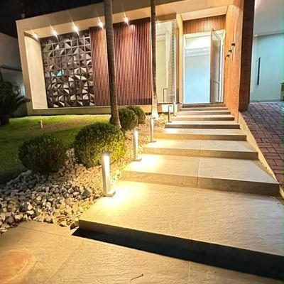 Entrada de residência moderna com iluminação externa, jardim bem cuidado.