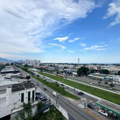 Visão de rua movimentada com prédios, árvores e céu parcialmente nublado.