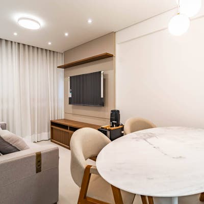 Sala de estar com cortinas brancas, sofá cinza, mesa de mármore.