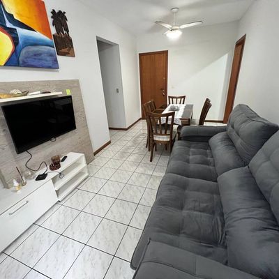 Sala com piso de cerâmica, paredes brancas, sofá cinza e televisão