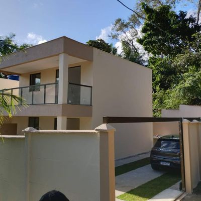 Fachada de residência moderna, parede lisa, varanda com vidro, árvores ao fundo