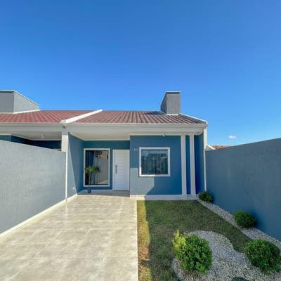 Casa com fachada azul, porta branca, janelas com cortinas sob céu claro