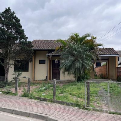Fachada de casa com árvores e muro de alvenaria, céu nublado