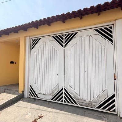 Fachada de casa com portão de madeira em acabamento branco e telhado de cerâmica.