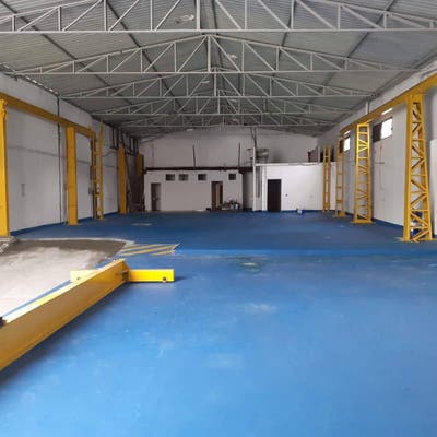 Espaço industrial com estrutura metálica, chão azul e paredes brancas.