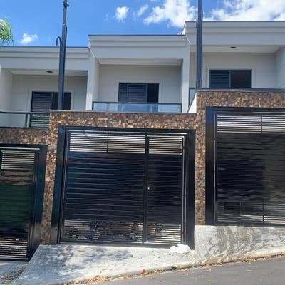 Fachada moderna com muro de pedras e portões de metal preto.