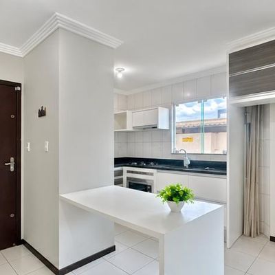Cozinha branca com balcão, armários brancos e janela grande