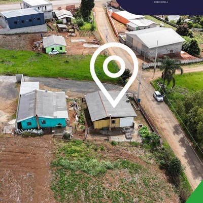 Área externa com casas, árvores e caminho de terra, vegetação ao redor.