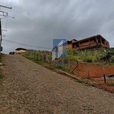 Estrada de pedra com casa em construção e vegetação ao redor.