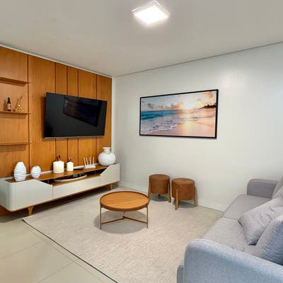 Sala com móvel de TV, quadro de praia e sofá cinza.